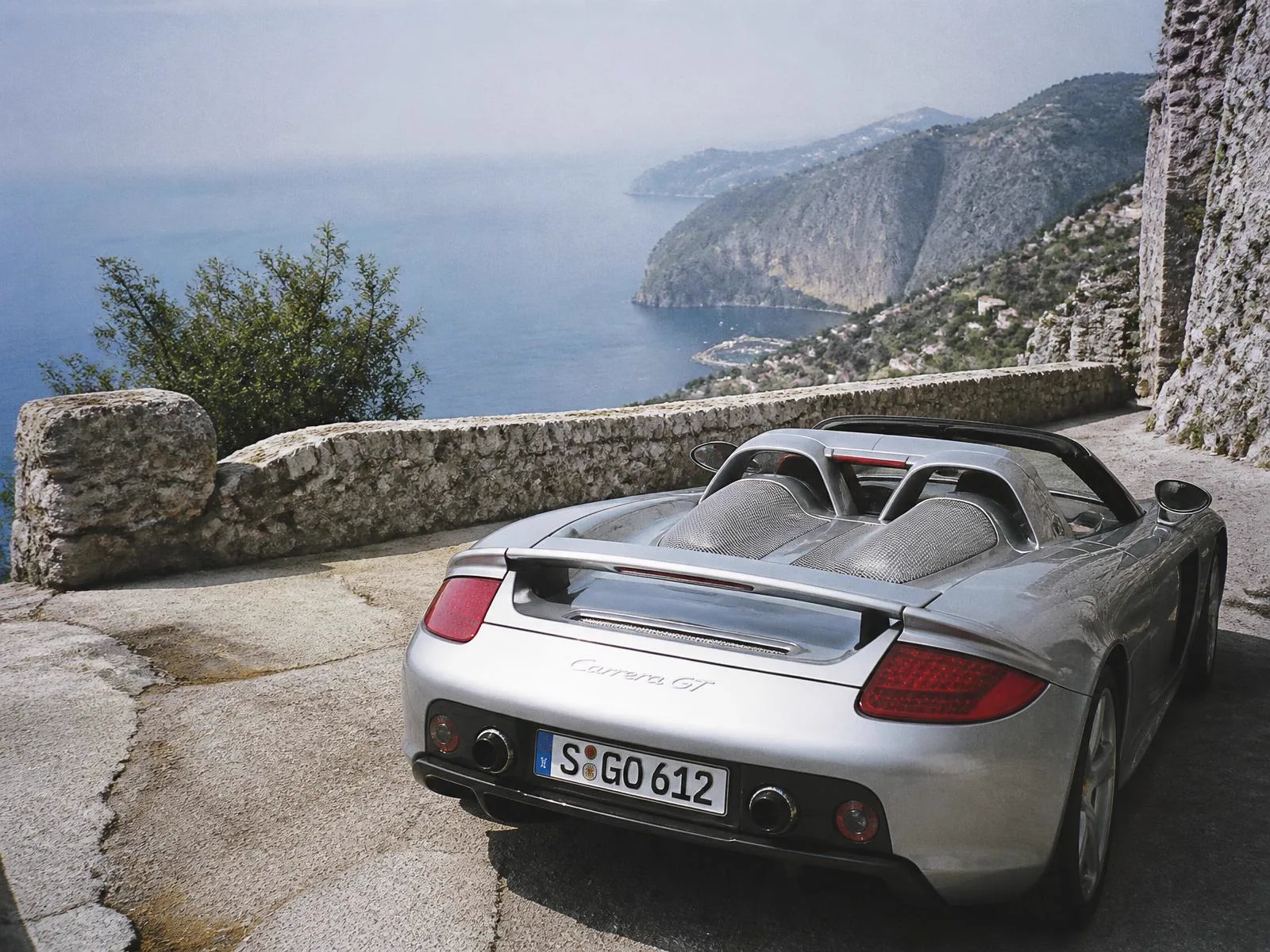 A silver Porsche Carrera GT on a cliff road above the coastline